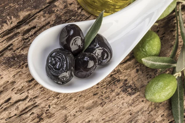 Green and black olives and olive oil on wooden table