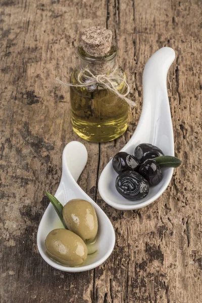 Green and black olives and olive oil on wooden table