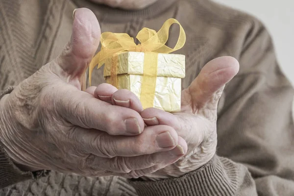 Pequeño regalo amarillo en la palma arrugada de una persona mayor —  Fotos de Stock