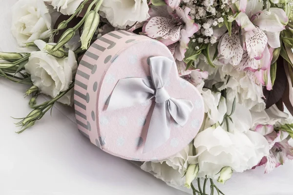 Herzförmiges Geschenk und Blumen auf weiß — Stockfoto