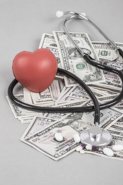 A stethoscope and a red heart on American Dollars on grey background