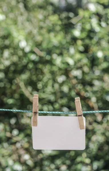 Papel branco vazio pendurado com pegs de roupas na corda no jardim — Fotografia de Stock