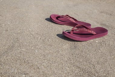 Kumlu bir plaj üzerinde kırmızı flip flop