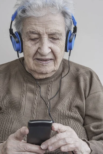 Senior woman listening music with headphones and smart phone