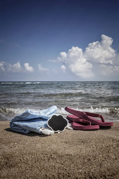 Καλοκαιρινό φόντο με σαγιονάρες και πετσέτα στην παραλία — Φωτογραφία Αρχείου
