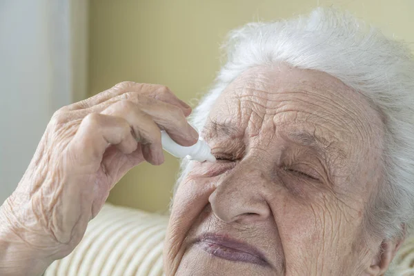 Una mujer mayor que se aplica gotas en los ojos sola — Foto de Stock