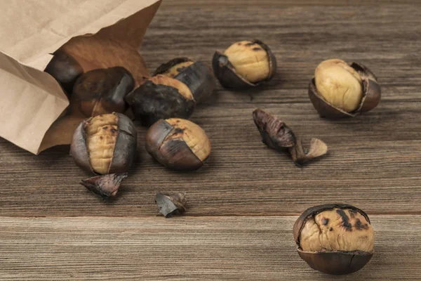 Geroosterde kastanjes in een papieren zak op een houten tafel — Stockfoto