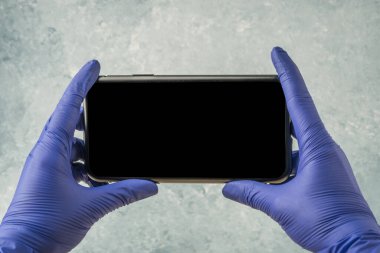 Eller mavi ameliyat eldiveni giyerken cep telefonunu boş ekranla tutuyor.