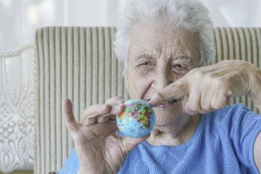 Yaşlı kadın kırışık elinde küçük bir küre gösteriyor.