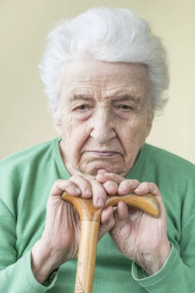 closeup of a sad old woman leaning on a wooden cane
