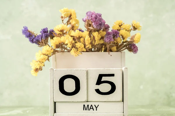 White cube calendar for may decorated with flowers over green background with copy space