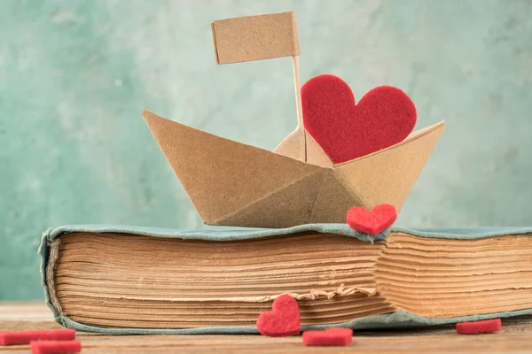 paper boat on an old book on table. Hand crafted origami paper sailing boat on book decorated with hearts.