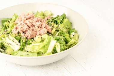 Taze yeşil salata ve ahşap bir masada bir kasede ton balığı.