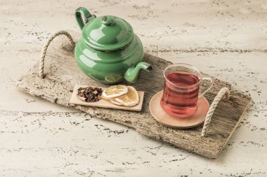 Bir bardak bitkisel çay ve ahşap bir masanın üzerinde eski bir mineli çaydanlık.