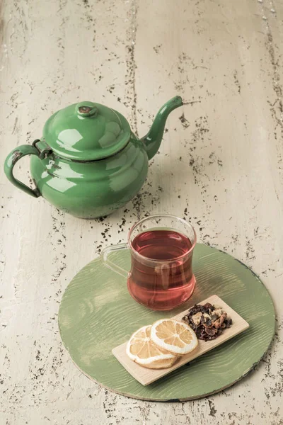 a glass of herbal tea and vintage enamel teapot on a wooden table