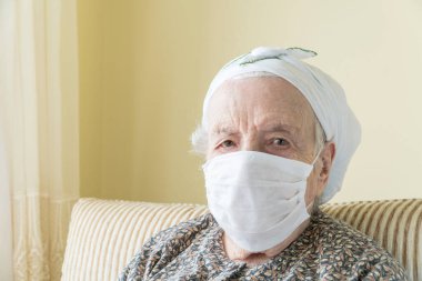 Evde kovid19 virüsünü korumak için tıbbi maske takan yaşlı kadın.