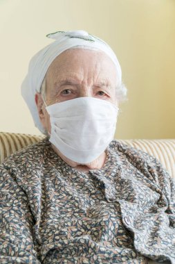 Evde kovid19 virüsünü korumak için tıbbi maske takan yaşlı bir kadın.