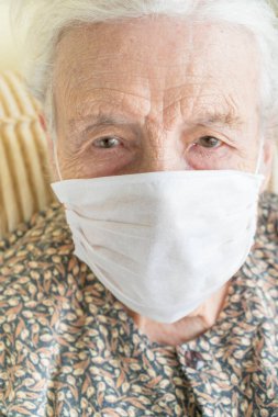 Kovid19 virüsünü korumak için tıbbi maske takan yaşlı bir kadın.