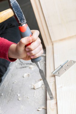 Bir çocuğun ellerinde keski ve çekiç, ahşap kapıya menteşeler takın.