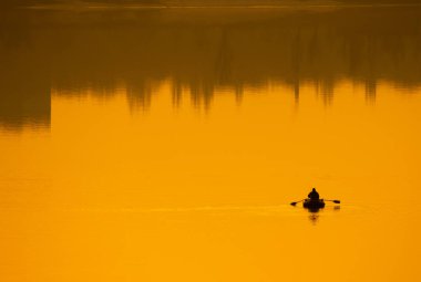 Teknede bir balıkçı. Tekne suya yansıyor.