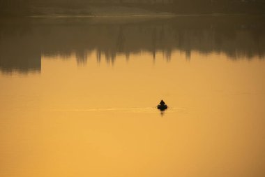 Teknede bir balıkçı. Tekne suya yansıyor.
