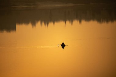 Teknede bir balıkçı. Tekne suya yansıyor.