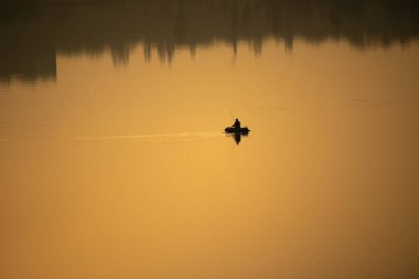 Teknede bir balıkçı. Tekne suya yansıyor.