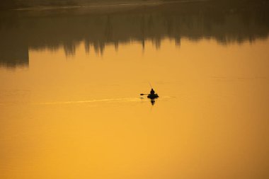 Teknede bir balıkçı. Tekne suya yansıyor.
