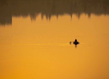 Teknede bir balıkçı. Tekne suya yansıyor.