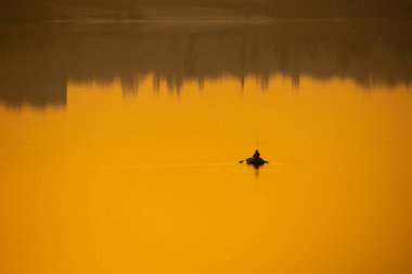 Teknede bir balıkçı. Tekne suya yansıyor.