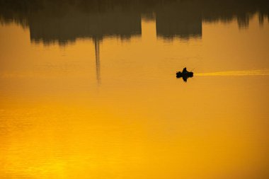 Teknede bir balıkçı. Tekne suya yansıyor.