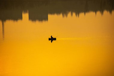 Teknede bir balıkçı. Tekne suya yansıyor.
