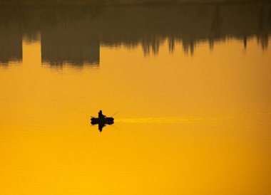Teknede bir balıkçı. Tekne suya yansıyor.
