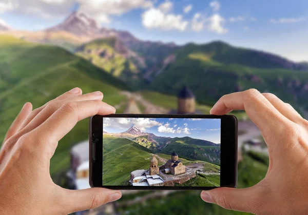 Concepto de viaje. Manos haciendo foto de la iglesia ortodoxa de Gergeti en las montañas, Georgia — Foto de Stock