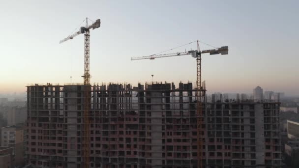 No fundo, guindaste de trabalho e cidade. Tiro aéreo do edifício no processo de construção. Trabalho trabalhando em grande canteiro de obras — Vídeo de Stock