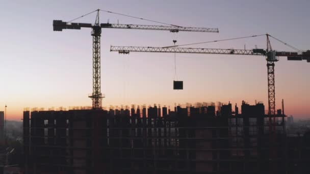 Flygfoto av byggnaden i byggprocessen. Arbete på en stor byggarbetsplats. I bakgrunden arbetande kran och stad. — Stockvideo