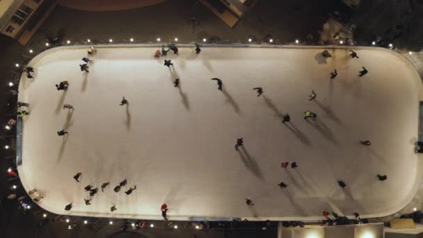 Les gens patinent sur la patinoire le soir. Vue aérienne verticale du haut vers le bas . — Video