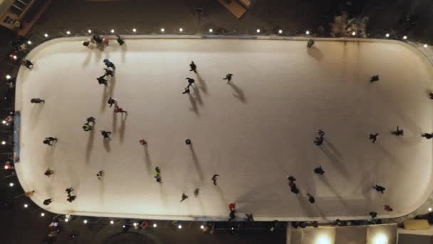 La gente pattina sulla pista di pattinaggio la sera. Vista aerea verticale dall'alto verso il basso . — Video Stock