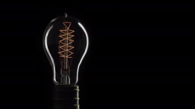 Gerçek Edison ampulü yanıp sönüyor. Klasik filament Edison ampulü. Kapatın. 4k Uhd videosu. Fikrin sembolü. Işık siyah bir arkaplanda yanar..