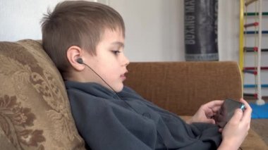 Çocuk kanepede akıllı telefondan çizgi film izliyor. Anaokulu öğrencisi cep telefonu çalıyor. Telefonu kullanan çocuk..