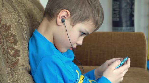 Niño viendo dibujos animados en el teléfono inteligente en el sofá. Preescolar jugando al teléfono móvil. Niño usando el teléfono . — Vídeos de Stock