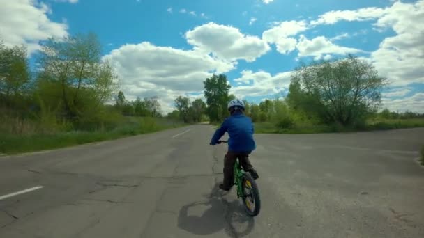 Ciclismo infantil. Niño montando una bicicleta en un casco en la carretera en los suburbios . — Vídeo de stock