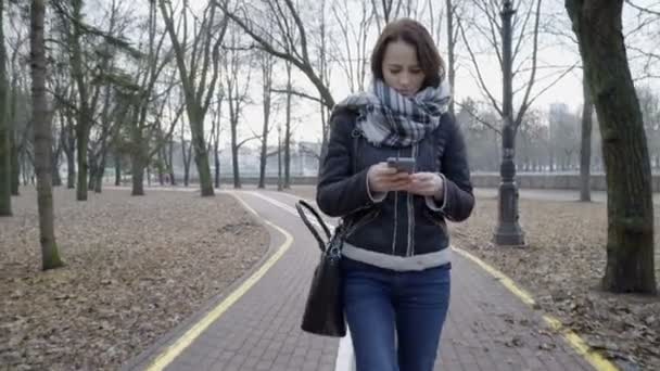 Женщина, гуляющая в городском парке со смартфоном — стоковое видео