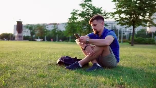 Ο άνθρωπος που κάθεται στο γρασίδι και και flipping smartphone — Αρχείο Βίντεο