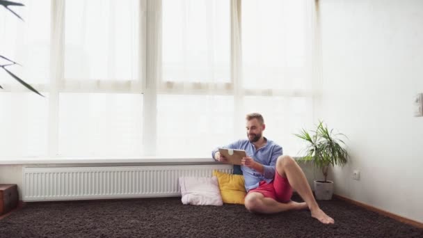 男子坐在地板上, 在家里使用平板电脑 — 图库视频影像