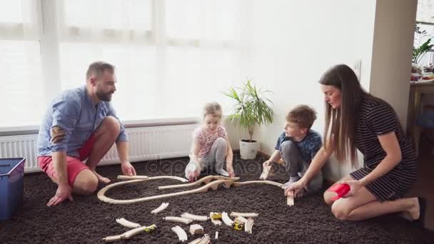 Madre y padre ayudan a sus hijos a construir un ferrocarril de juguete — Vídeo de stock