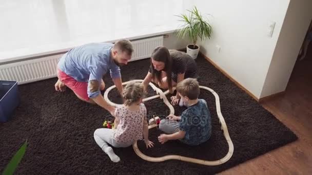 Menino e menina juntos com pai e mãe construir uma ferrovia brinquedo — Vídeo de Stock