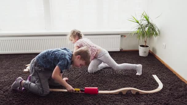 Kinderen bouwen een smalspoorlijn speelgoed in een kamer op de vloer — Stockvideo