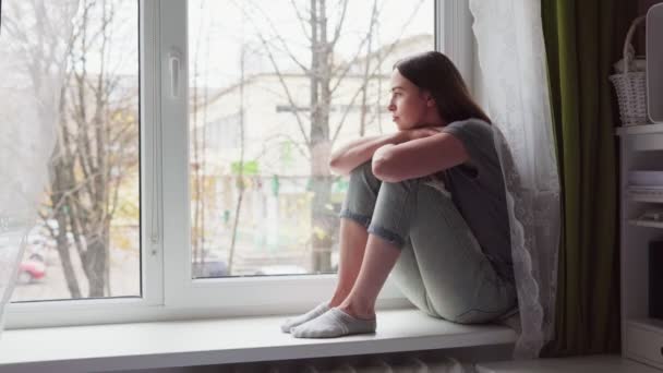 Sorgliga kvinna sitter på fönsterbrädan och ser på en mulen höstdag — Stockvideo