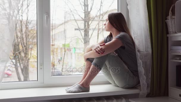 Femme triste s'assoit sur le rebord de la fenêtre, regarde par la fenêtre et abaisse la tête sur les genoux — Video